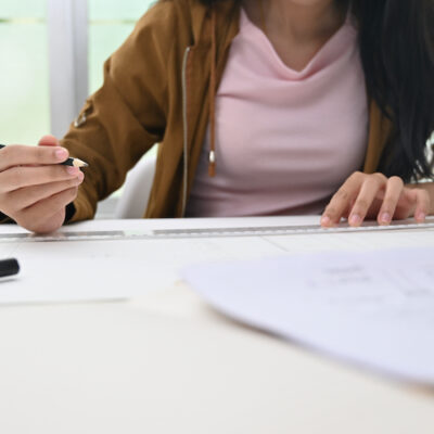 Close-up caucasian female architect drawing on blueprint with creative workspace.